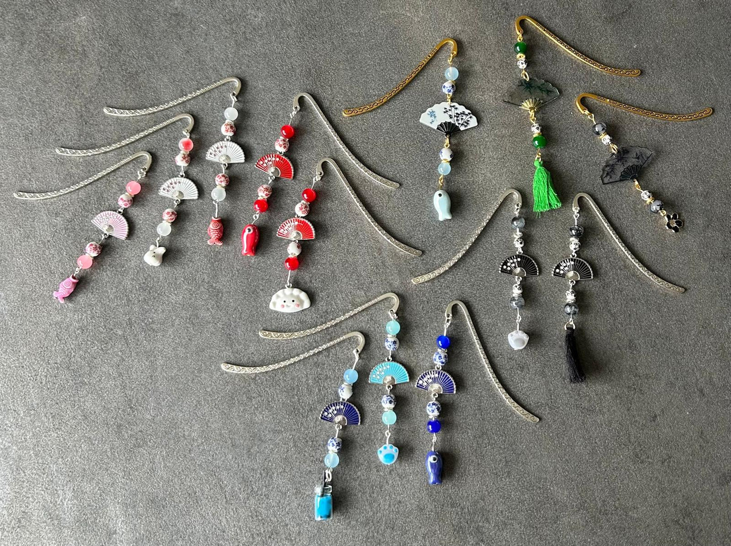 Une série de marque‑pages métalliques ornés de perles, éventails et petits charms colorés. Alignés par teintes, ils évoquent l’artisanat asiatique et la délicatesse des objets faits main.